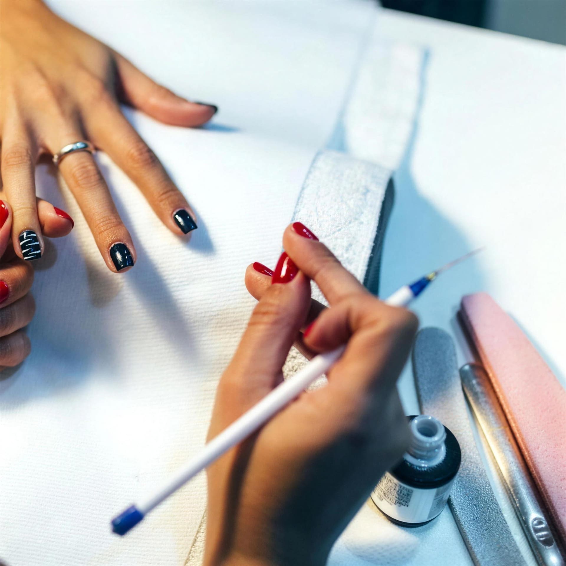 Twee handen aan het werk tijdens een manicure: een fijn penseel brengt rode nagellak aan, met gelakte nagels en gereedschap binnen handbereik.