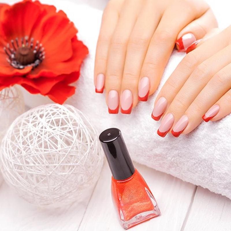 Een rode nagellak, een witte handdoek en een rode bloem: de rust van een manicurebehandeling.